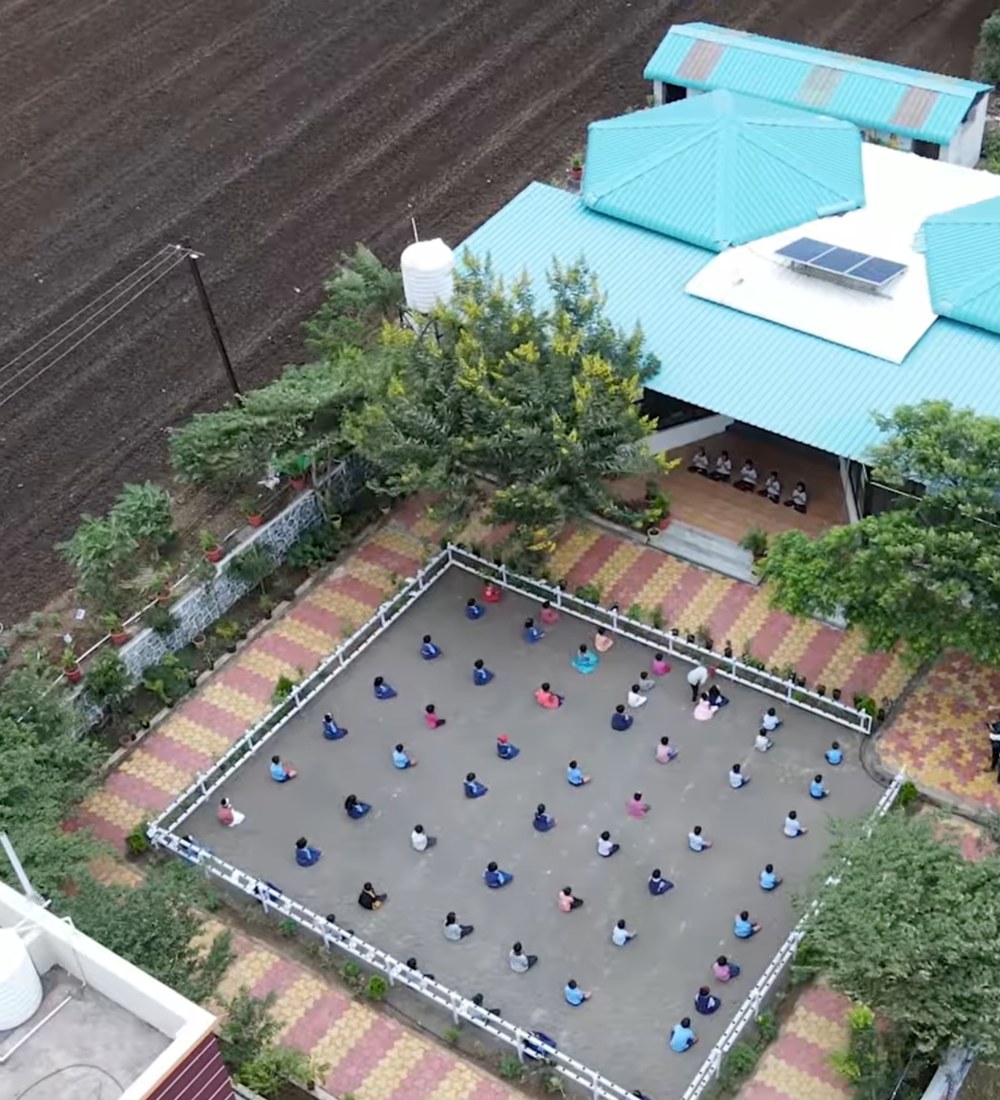 Aerial view of a transformed school: students seated in the courtyard beside the rebuilt classrooms